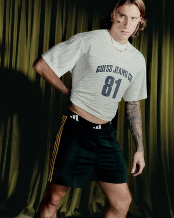 Riccardo Calafiori posing in a white mesh jersey t-shirt and dark athletic shorts against olive green pleated drapery.