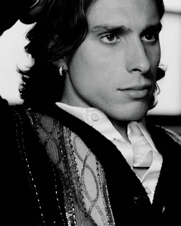Black and white close-up portrait of Riccardo Calafiori wearing an embellished patterned knit cardigan and a white collared shirt.