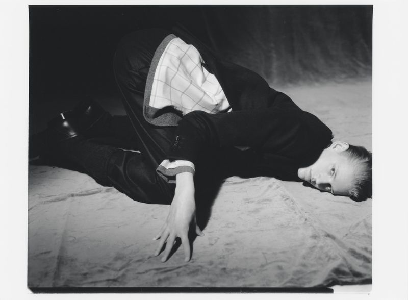Monochrome portrait of a person in a jacket reclining on a surface, with a focus on their face and clothing details.