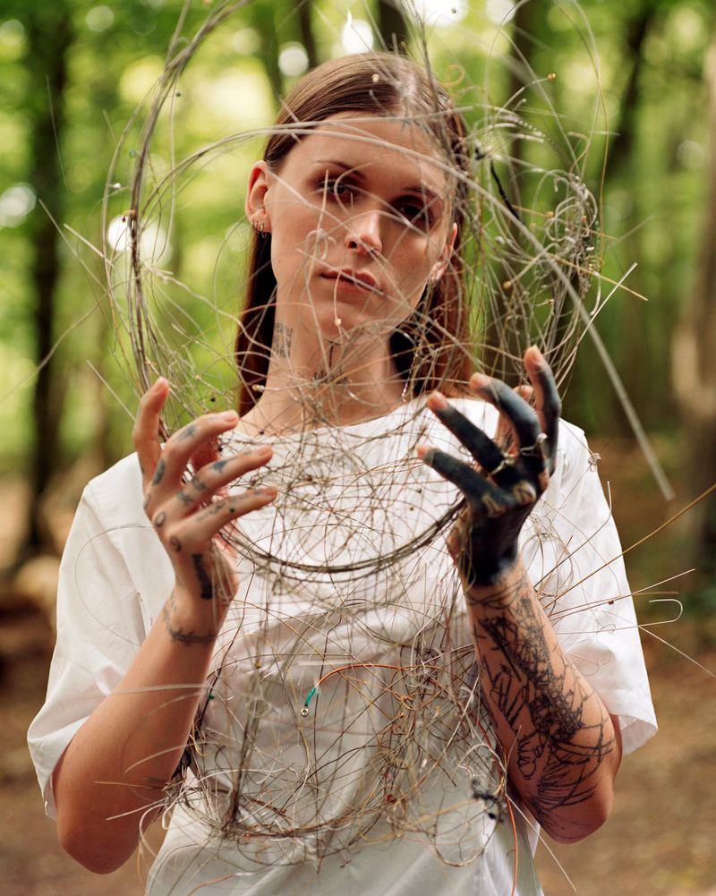 Young woman poses with wire art in outdoor forest setting. Portrait of female artist in nature with handmade wire sculpture.