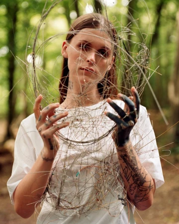 Young woman poses with wire art in outdoor forest setting. Portrait of female artist in nature with handmade wire sculpture.