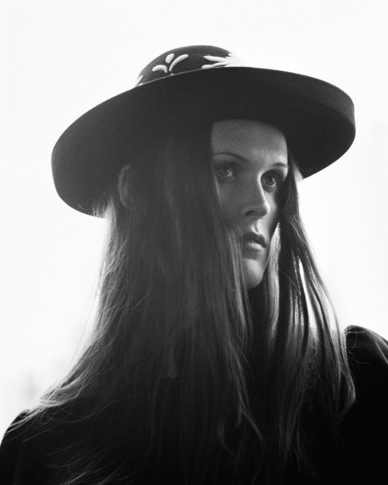Black and white portrait of a long-haired woman wearing a wide-brimmed hat, captured with soft lighting, evoking a vintage aesthetic.