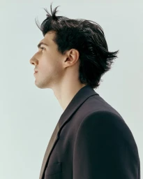 Profile portrait of a man with dark hair wearing a dark blazer against a plain light background