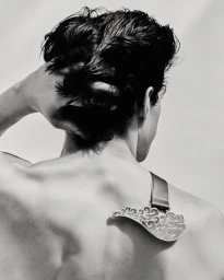 Monochrome rear view portrait of a man touching his dark wavy hair wearing a decorative metal shoulder ornament