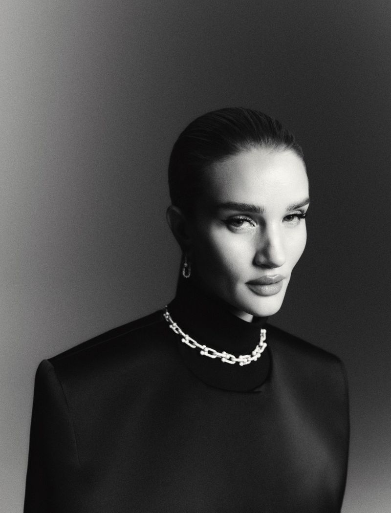 Black and white portrait of a woman wearing a black turtleneck, silver necklace, and earrings against a simple background.