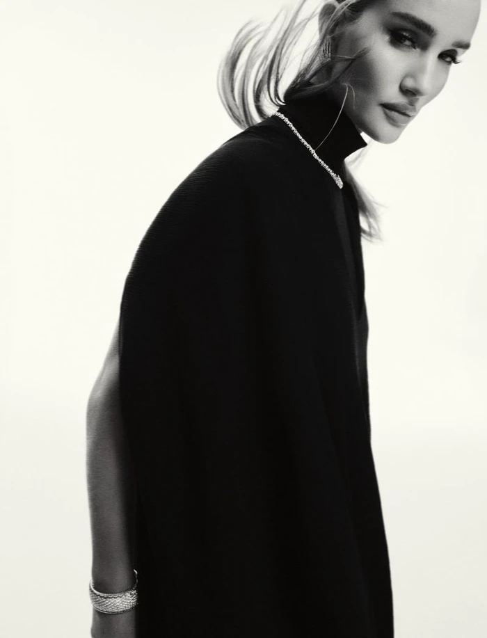 Rosie Huntington-Whiteley in a black high-neck top and silver jewellery posing against a white studio background.