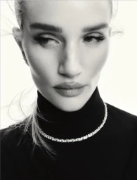 Close-up monochrome portrait of Rosie Huntington Whiteley wearing a dark turtleneck and diamond tennis necklace against a white background.