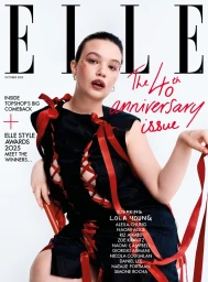 Woman in a black dress laced with red ribbons seated against a bright white background for an Elle UK cover.