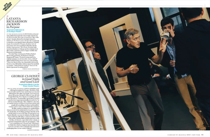 Candid moment of George Clooney conversing on a film set with crew members, featuring film equipment and set construction visible in the background.