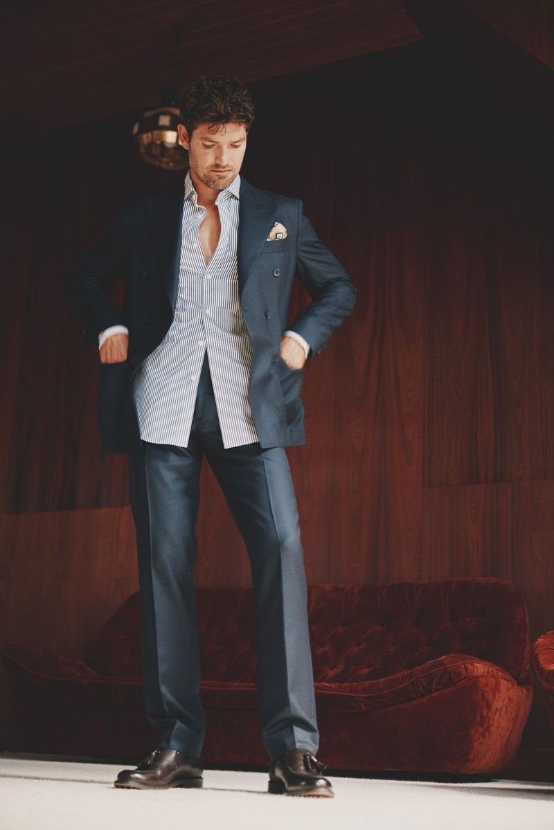 Adult male in a blue suit and striped shirt poses indoors with a red sofa. A disco ball hangs in the dimly lit background.