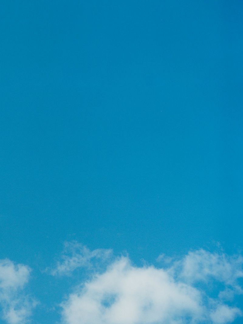 Vast expanse of bright blue sky fills the frame, with soft, fluffy white clouds clustered near the bottom, creating a serene skyscape.