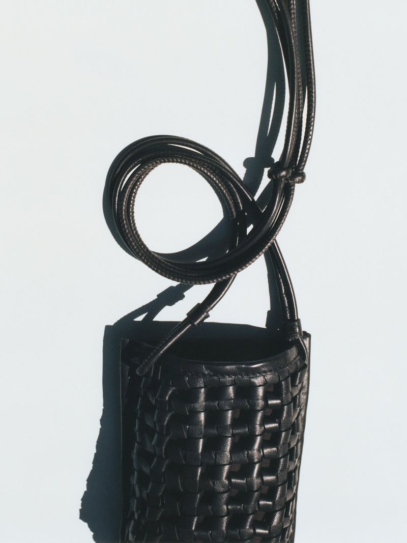 Woven leather crossbody bag in black, showcasing textured pattern and elegant design against a soft, neutral backdrop.