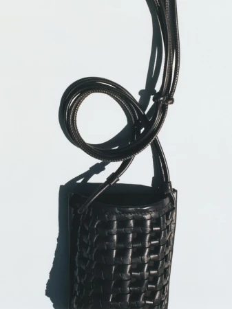 Woven leather crossbody bag in black, showcasing textured pattern and elegant design against a soft, neutral backdrop.