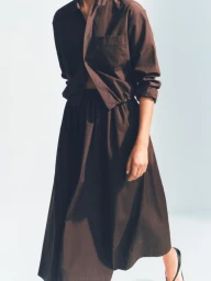 Model wearing a dark brown button-up shirt and matching brown full midi skirt with black sandals against a white studio background.