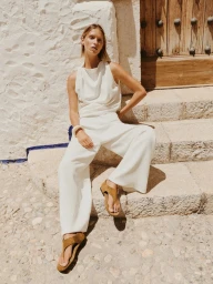 Model in white sleeveless top and wide-leg trousers wearing brown sandals on stone steps