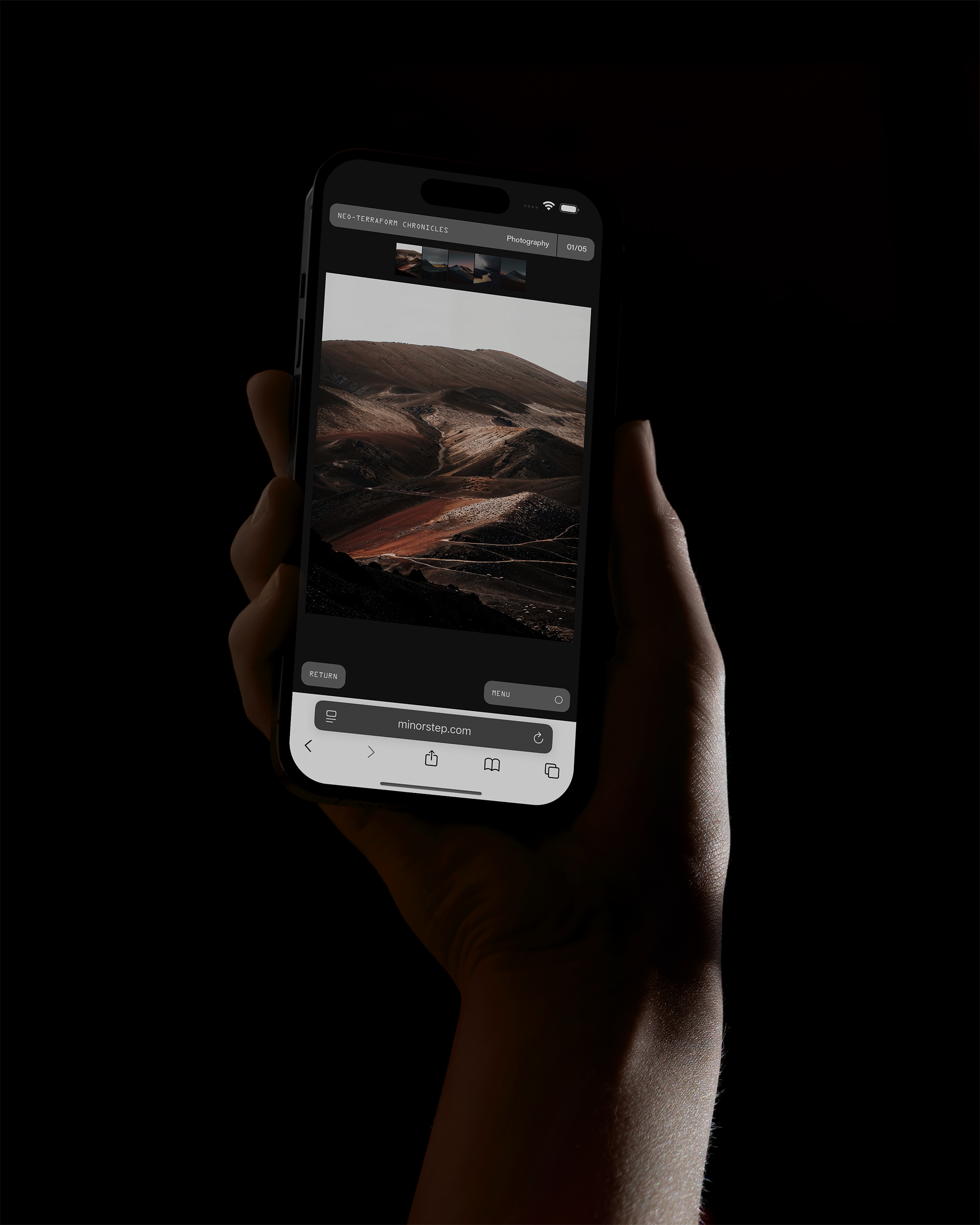 Hand holds a phone displaying a landscape photo. The screen displays desert terrain and brown mountains under a grey sky in muted tones.