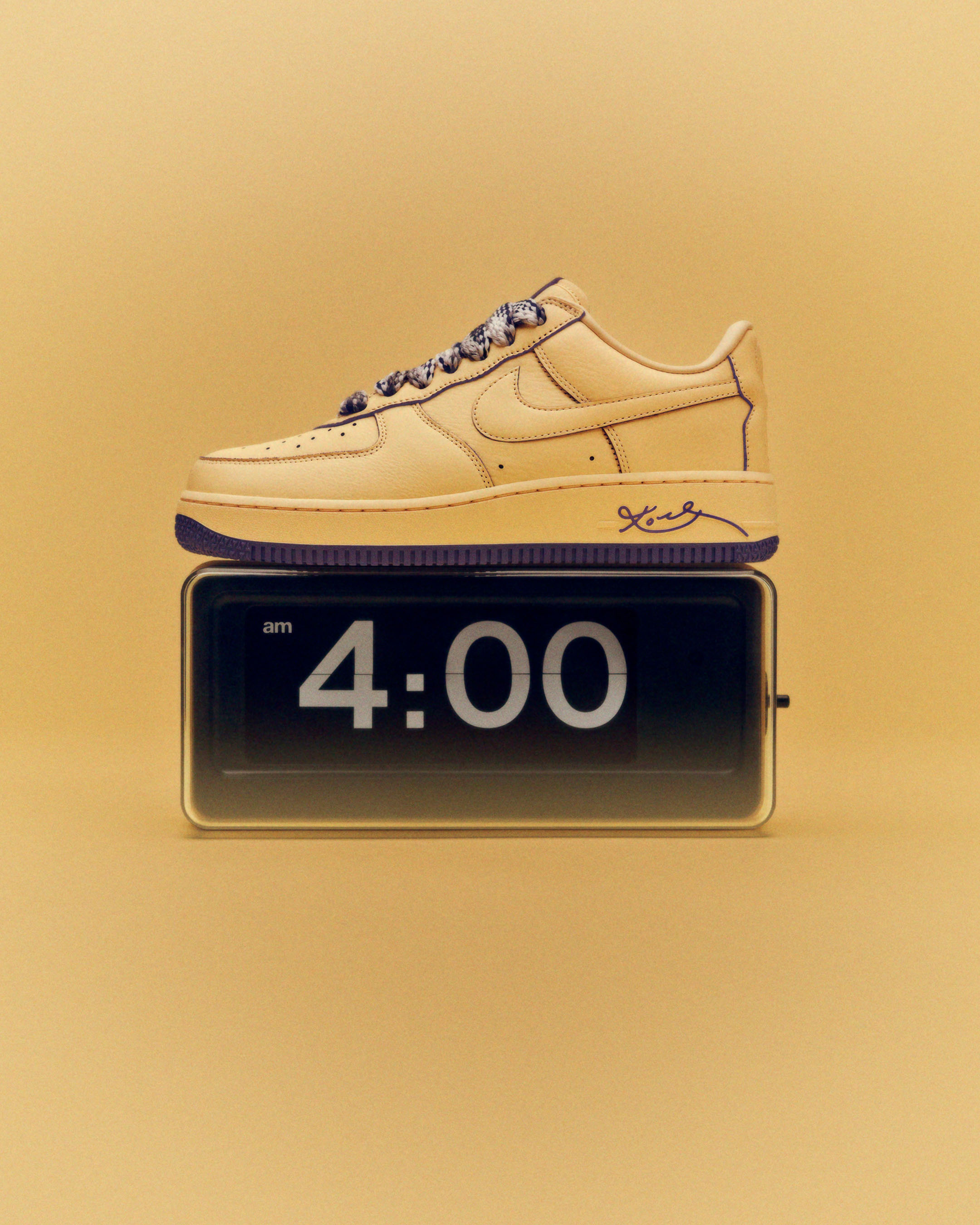 Tan Nike Air Force 1 sneaker with purple accents atop a retro digital clock displaying 4:00 AM, set against a tan backdrop.