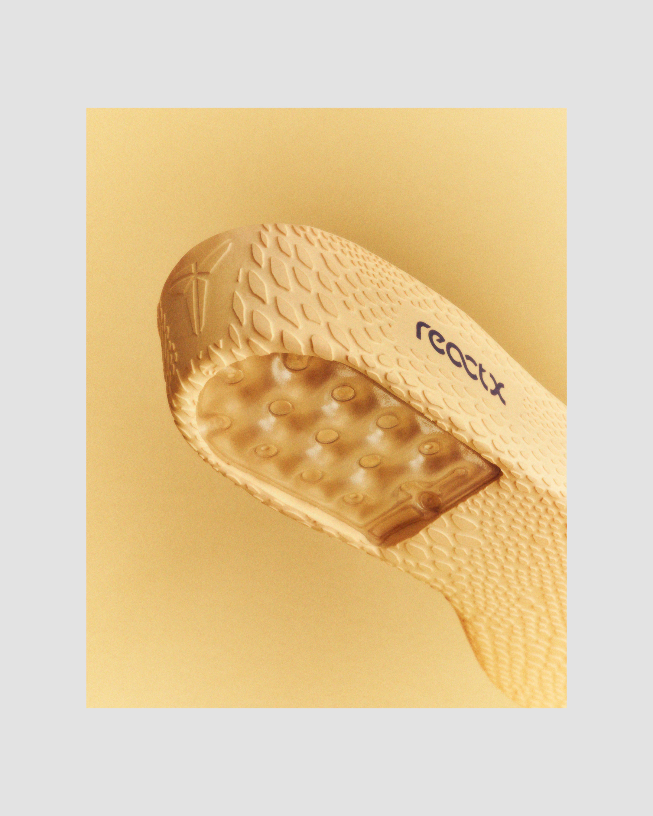 Angled shot of the sole of a light brown sneaker with a textured grip and visible 'reactx' logo, set against a light yellow background.