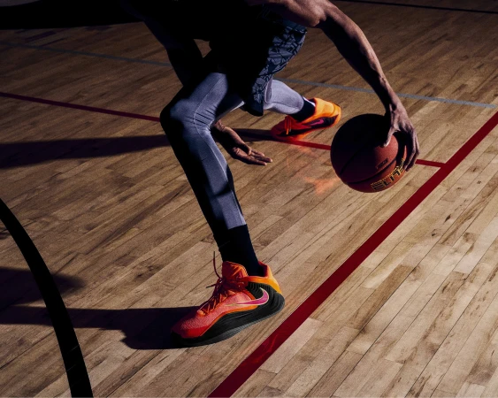 A basketball player in athletic wear dribbles a basketball on a wooden court with red lines, capturing a dynamic sports scene.