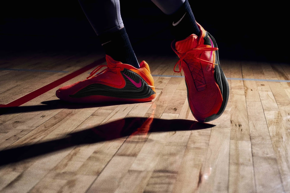 Low-angle shot of red Nike basketball shoes on a hardwood court, featuring a black swoosh and a man in gray socks.