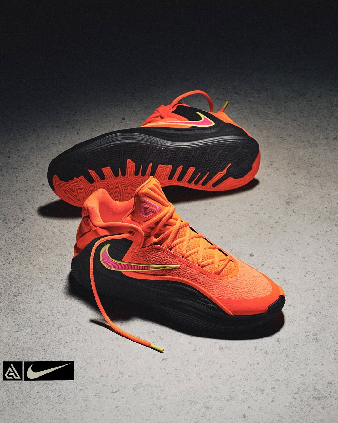Two orange and black athletic shoes are displayed against a mottled gray background, emphasizing the design and texture.