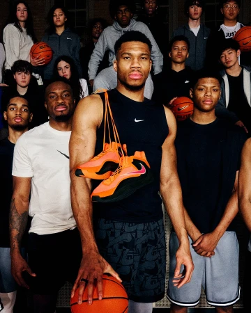 Group shot with basketball player Giannis Antetokounmpo, holding a basketball and his orange sneakers, surrounded by a group of people.