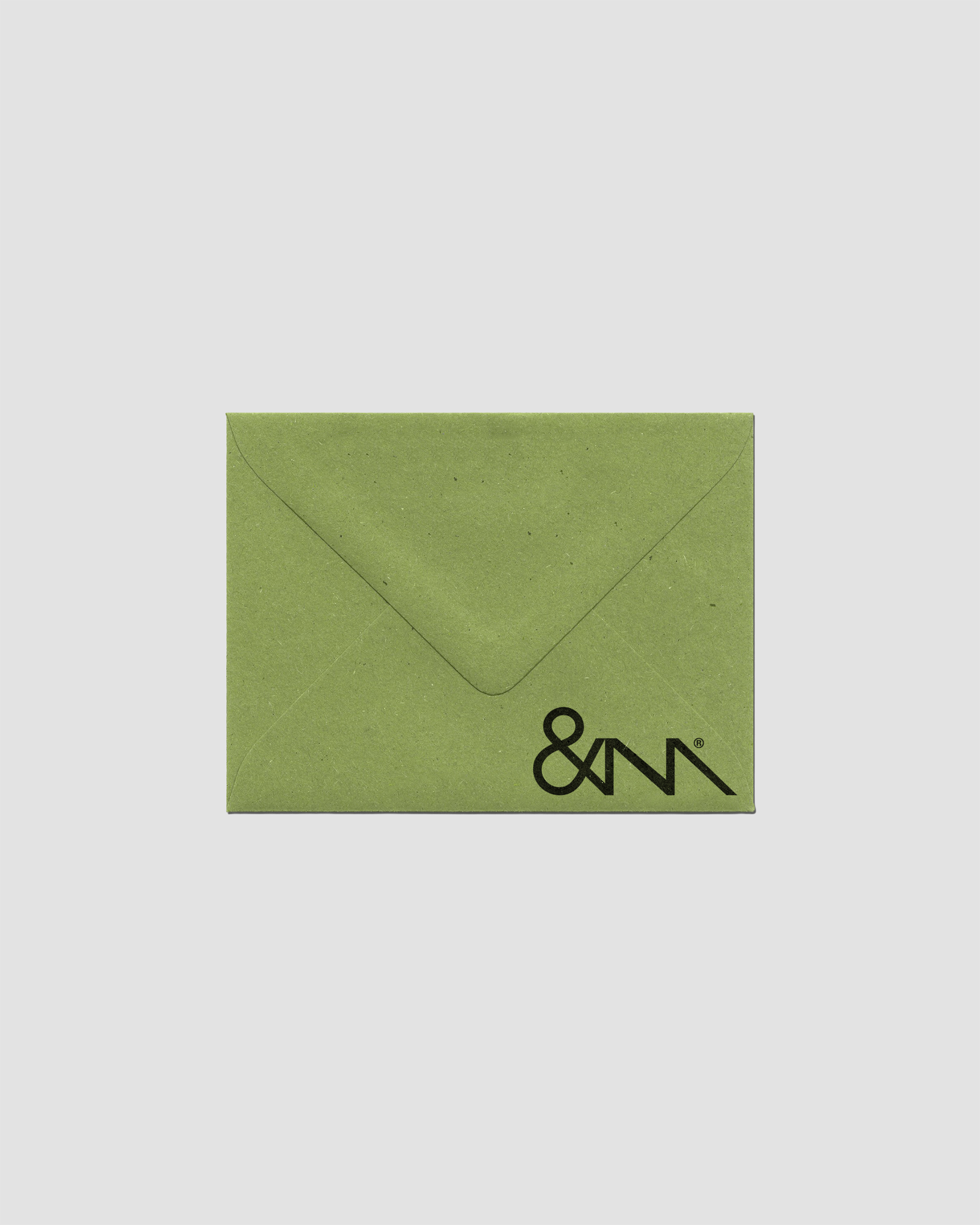 Close-up of a light green envelope with a simple logo in the lower corner, set against a neutral gray background in portrait layout.