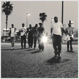 Group of men walking across a paved parking lot at night with palm trees in the background under streetlights.