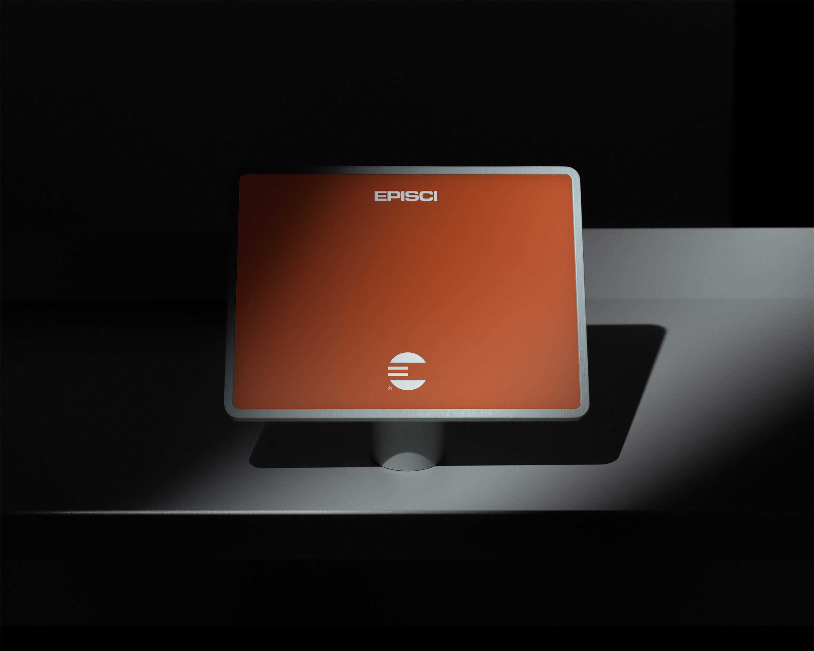 Minimalist product display featuring an orange screen on a white pedestal, illuminated by a spotlight against a dark gray backdrop.