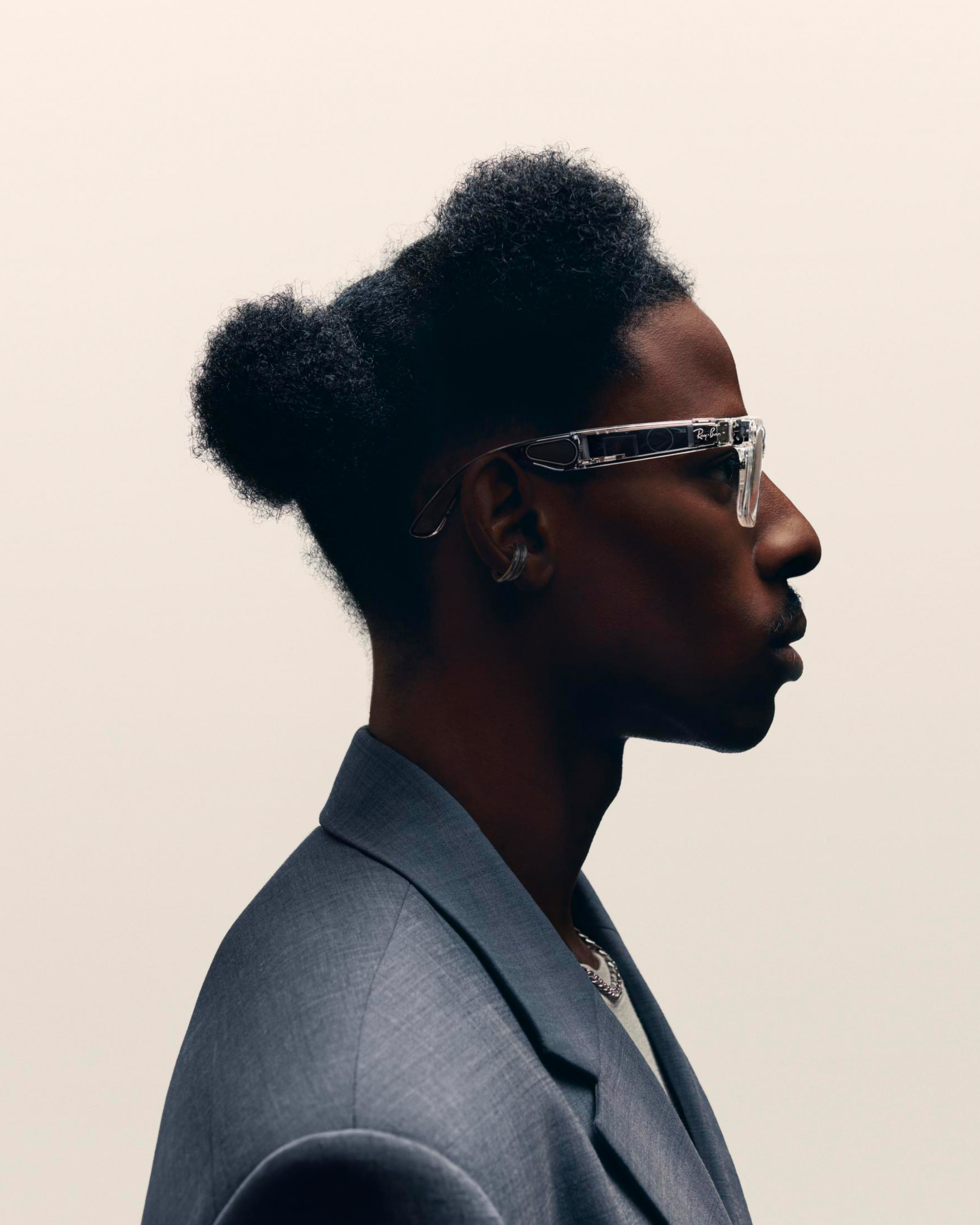 Portrait of a Black man in a gray suit and clear glasses looking up against a cream background in a brightly lit, high-angle shot.