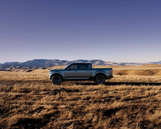 Silver pickup truck parked in a field with mountains in the background under a blue sky. Automotive vehicle, rural environment.