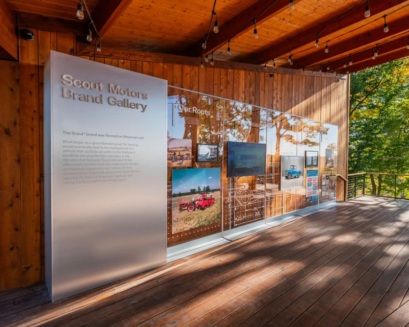 Scout Motors Brand Gallery exhibit featuring vintage automobile imagery, visible through clear panels, set on a wooden platform.