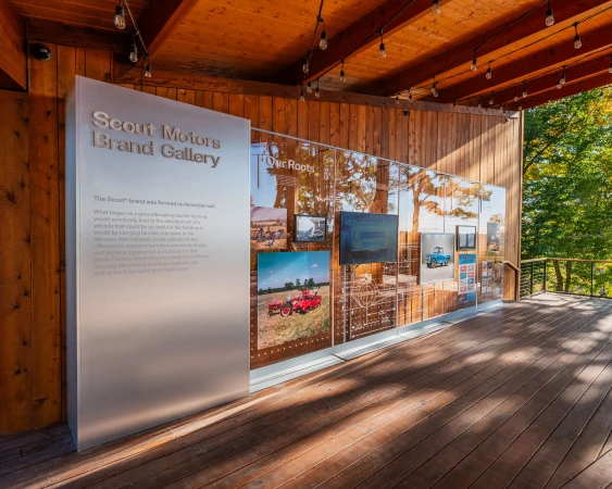 Scout Motors Brand Gallery exhibit featuring vintage automobile imagery, visible through clear panels, set on a wooden platform.