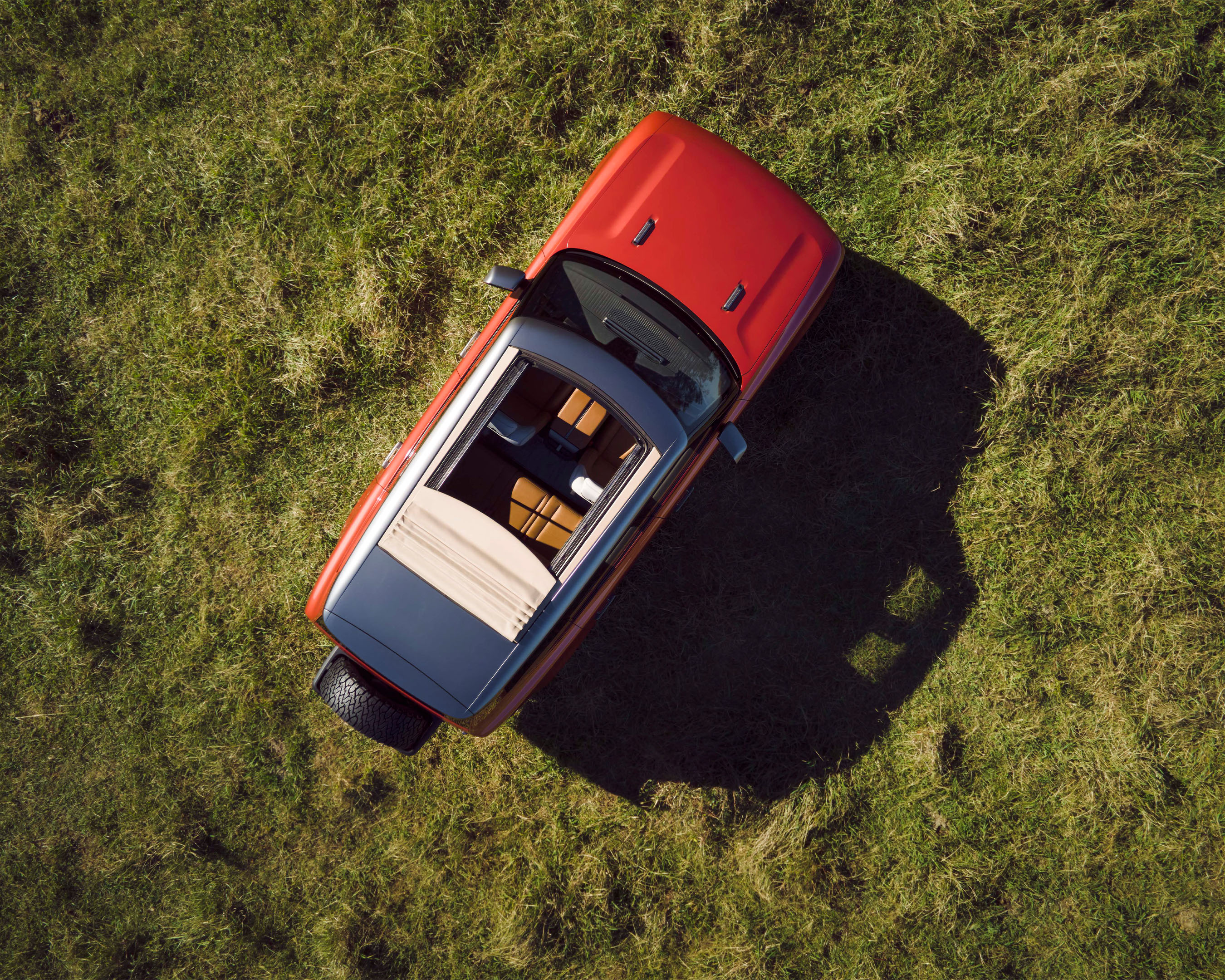 Aerial view of a red and gray four-door SUV parked on a grassy field with visible car seating and a modern aesthetic design.