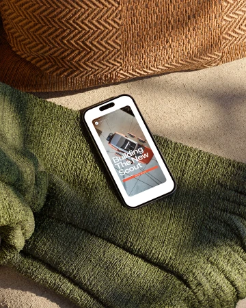Smartphone displays an advertisement for the new Scout vehicle; close-up shot with a textured throw and cushion in the background.