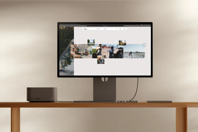 Computer monitor displaying digital photos, next to a desktop computer and keyboard on a light wood table against a neutral wall.