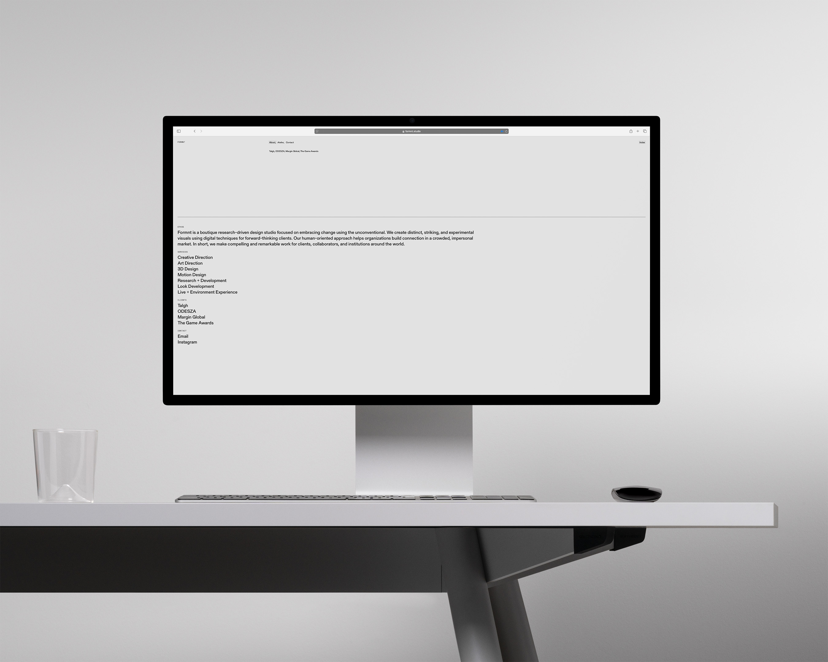 Computer monitor displaying a webpage with text, sitting on a white desk with a clear glass, a mouse, and a light grey background.