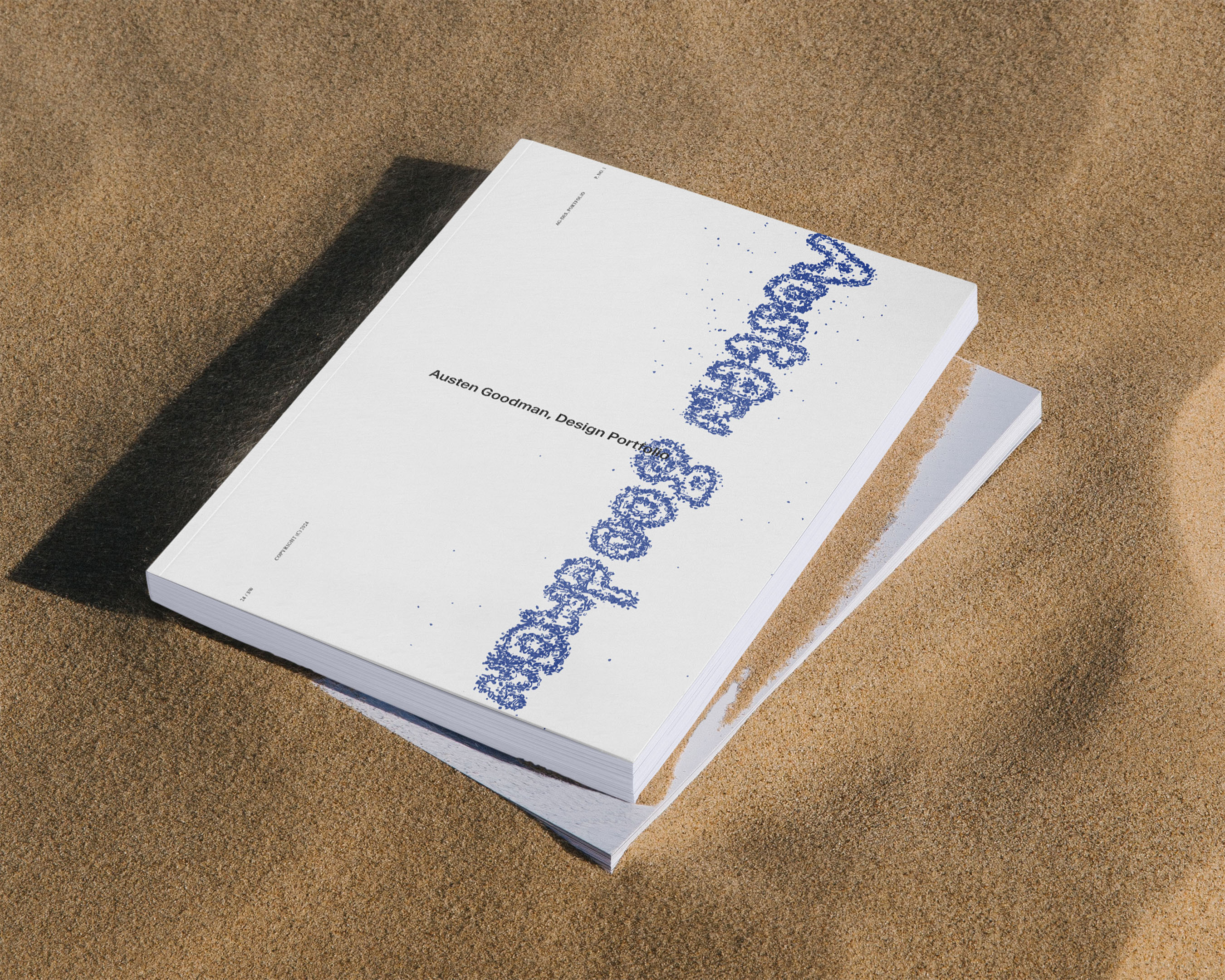 Stack of white books with blue stylized text on a sand surface in an outdoor setting with bright, diffused lighting.