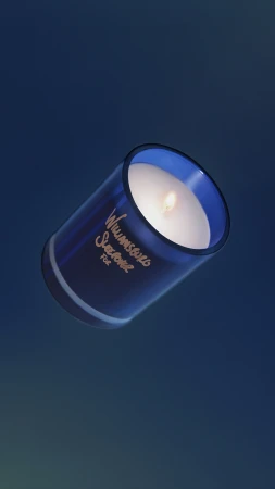 A lit scented candle with white wax in a translucent blue glass vessel floating diagonally over a deep blue gradient background.