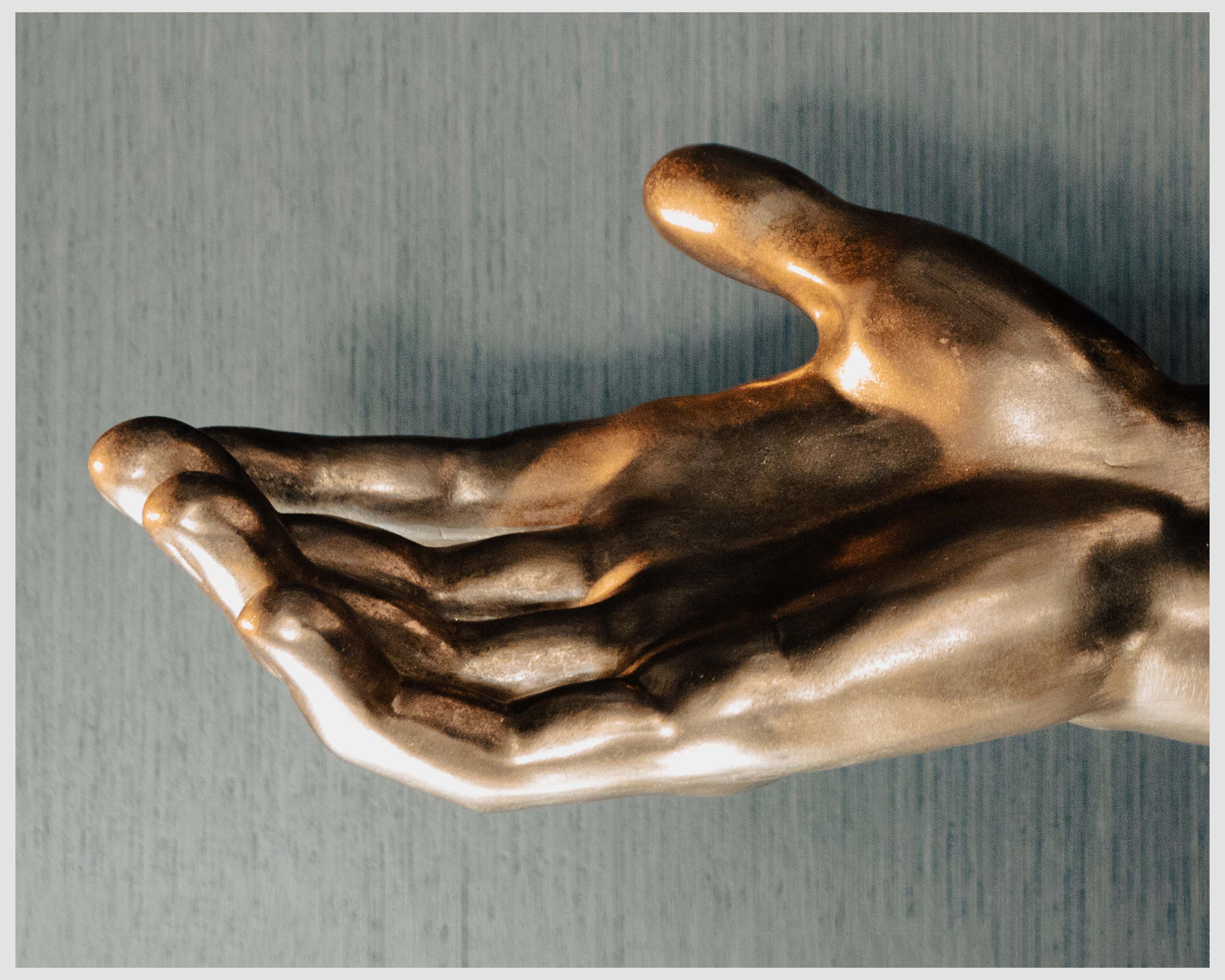 Close-up of a bronze-colored hand sculpture with an open palm set against a textured blue background, creating an artistic and inviting display.