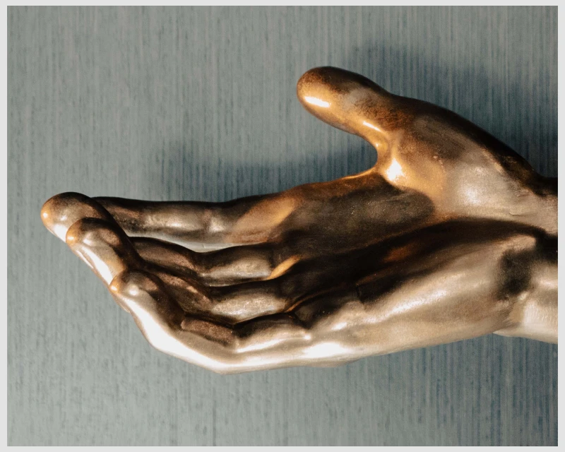 Close-up of a bronze-colored hand sculpture with an open palm set against a textured blue background, creating an artistic and inviting display.