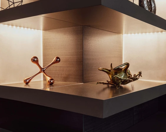 Corner shelf with bronze decorative objects. One is a jack-like shape and another is a sculptural piece; warm lighting highlights textures.