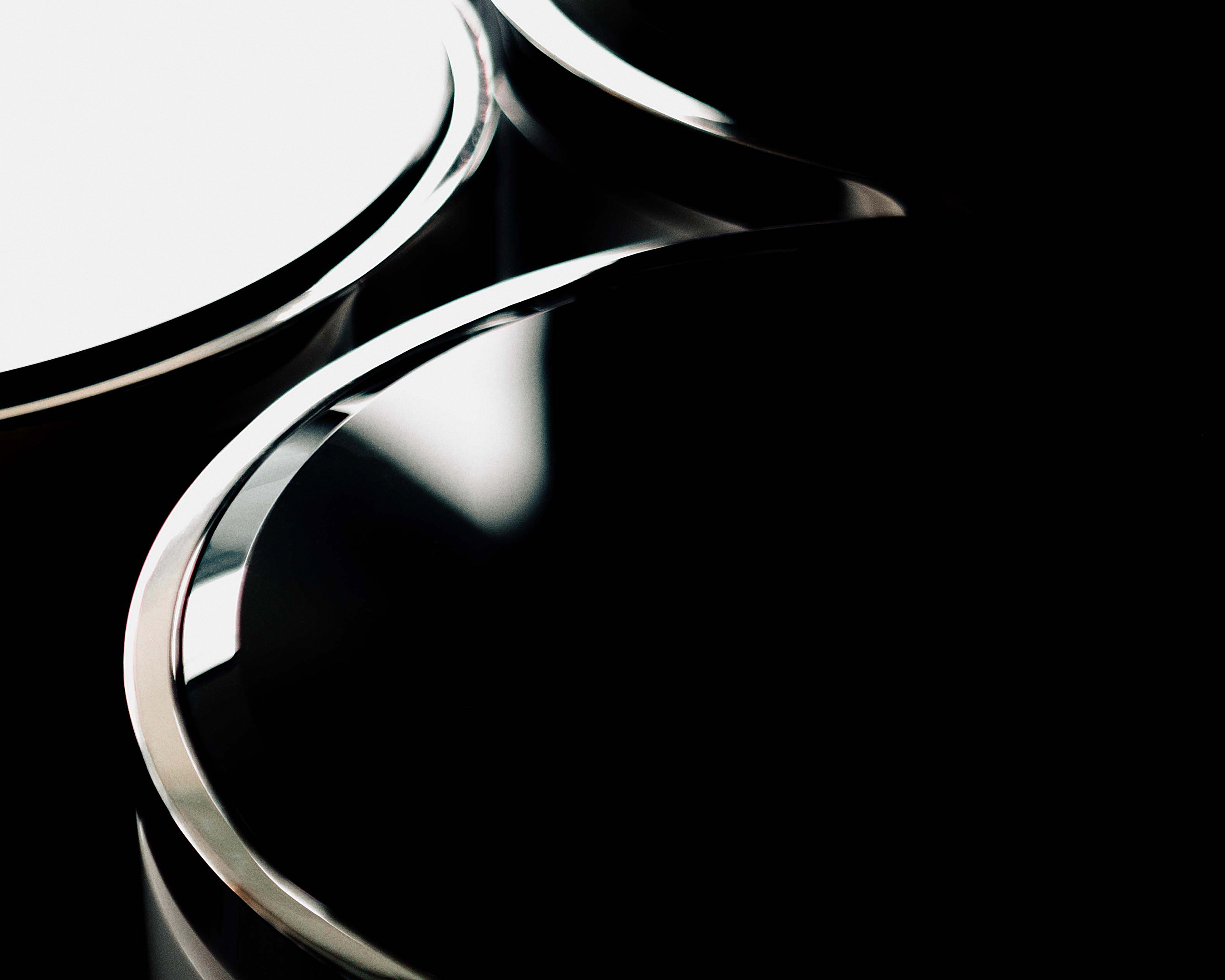 Abstract minimalist shot: Curved chrome lines contrast against a solid black backdrop. Modern design evokes sleekness and sophistication.