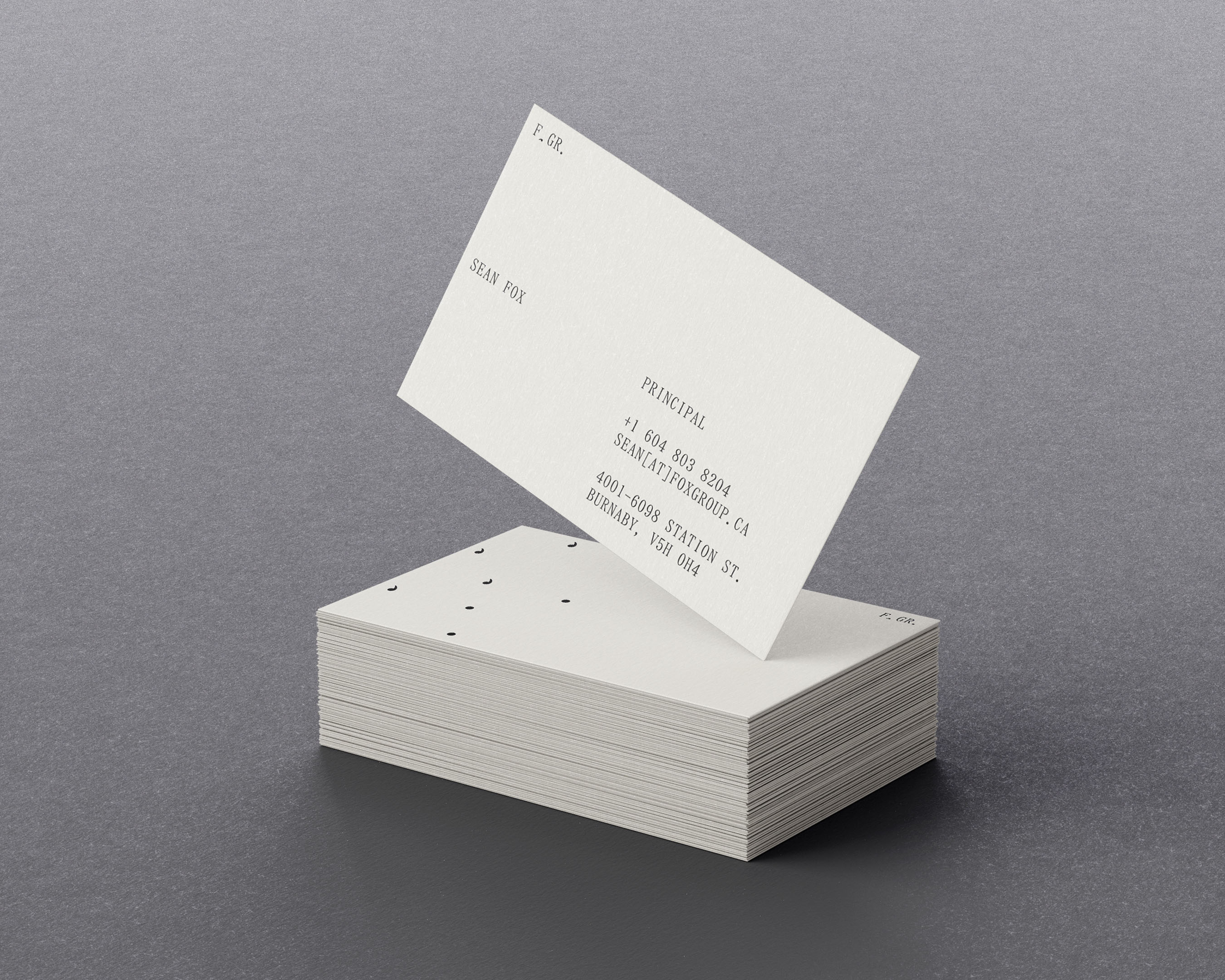 Stack of white business cards with black text on a gray background, one card angled on top revealing contact information.