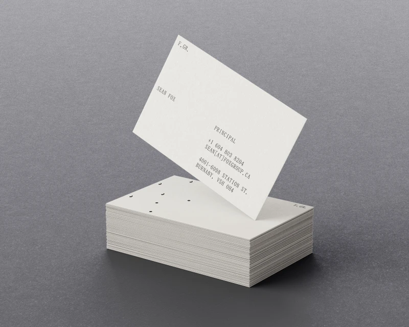 Stack of white business cards with black text on a gray background, one card angled on top revealing contact information.