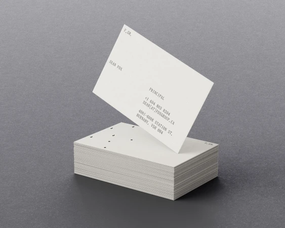 Stack of white business cards with black text on a gray background, one card angled on top revealing contact information.