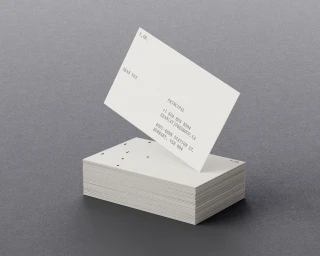 Stack of white textured business cards with minimalist black typography and dot perforations on a dark grey surface.