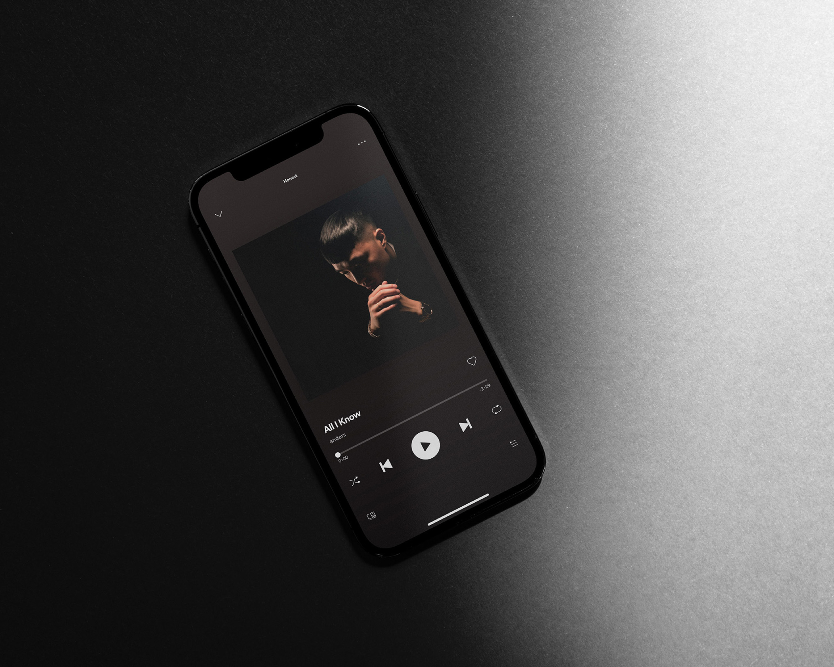 Mobile phone displays album art with portrait of a man with folded hands in dark lighting, set against a dark background.