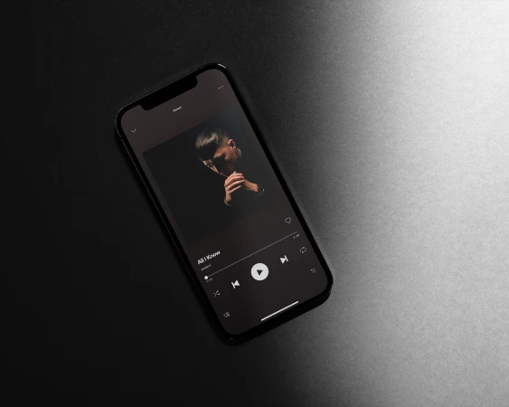 Mobile phone displays album art with portrait of a man with folded hands in dark lighting, set against a dark background.