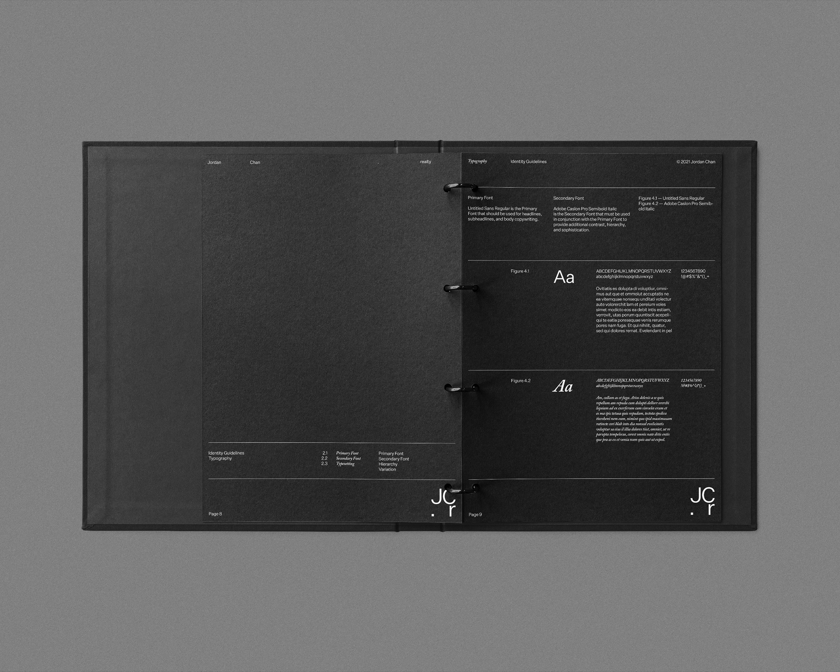 Open black ring binder with typography design and text on interior pages, laying on a grey surface in studio setting.